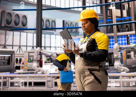 Female technician oversees robotic arms and automated systems, ensuring operational efficiency in industrial plant. Engineer controls green technology production line, upgrading industry 4.0 software. Stock Photo