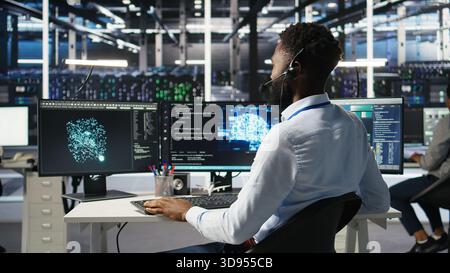 Data center employee talking in headset mic, coordinating technicians setting up hardware for artificial intelligence deployment. Server room worker engages in remote call with engineers, camera A Stock Photo