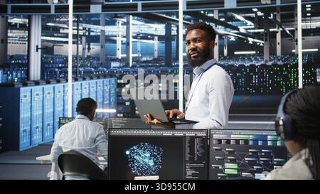 Portrait of cheerful data center engineer analyzing gear issues using node tree tools. Upbeat African american server hub specialist using AI visualization insights to optimize system health, camera A Stock Photo