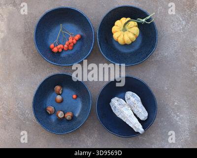 Rustic Blue Ceramic Bowls with Autumn Harvest: Rowans, Hazelnuts, Pumpkin, and Dried Root Vegetables. A top-down view captures four unique, deep blue Stock Photo