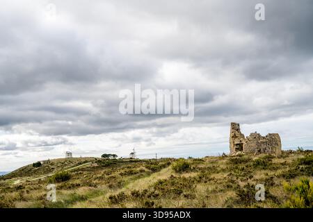 Alenquer Portugal November 29 2025. A ruined stone structure faces distant windmills across grassy hills on the Montejunto ridge Stock Photo