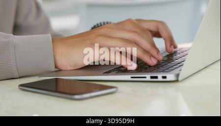 Typing male hands on silver laptop with visible ports at home, phone face-up, knit-sleeve wristband Stock Photo