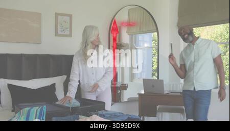 Packing senior woman arranging blouse on bed in bedroom, with open suitcase and red AR overlay Stock Photo