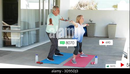 Practicing senior couple holding forward stance on covered patio in workout with mats, social icons Stock Photo