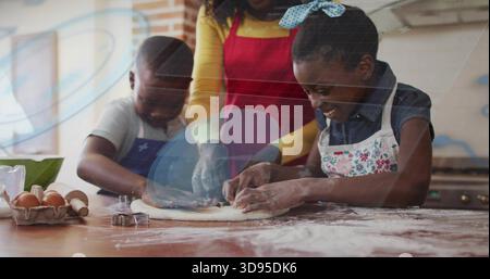 Guiding mother in red apron helping children shape flat dough in home kitchen with cookie cutters Stock Photo