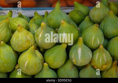 Close-up of plump green figs with smooth skin, teardrop shape, and subtle blemishes, displayed beside citrus fruits Stock Photo