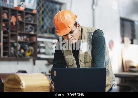 Carpenter using a laptop at a workbench in the workshop. Successful worker using a computer in the carpentry workshop Stock Photo