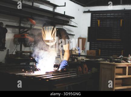 Deaf man using a welding torch in the workshop. Professional welder working at the workbench Stock Photo