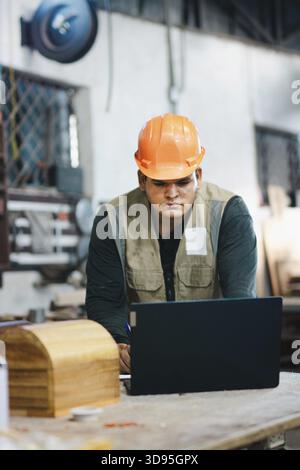 Successful worker using a computer in the carpentry workshop. Carpenter using a laptop at a workbench in the workshop Stock Photo