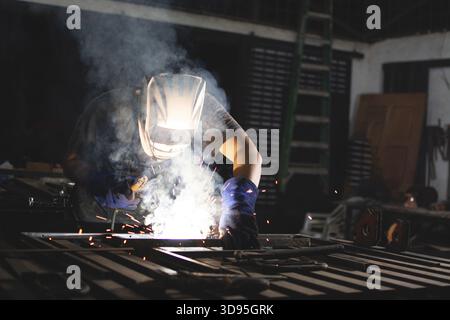 Professional welder working at the workbench. Deaf man using a welding torch in the workshop Stock Photo