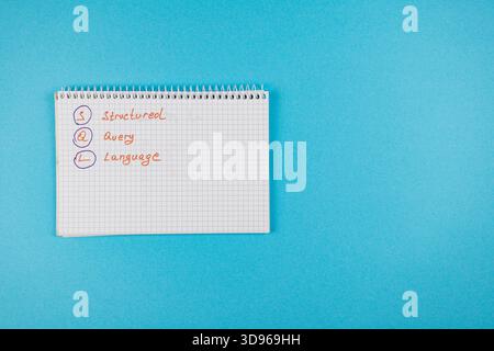 Handwritten notes on a notepad explain the concept of Structured Query Language on a bright blue background, highlighting its importance in programmin Stock Photo