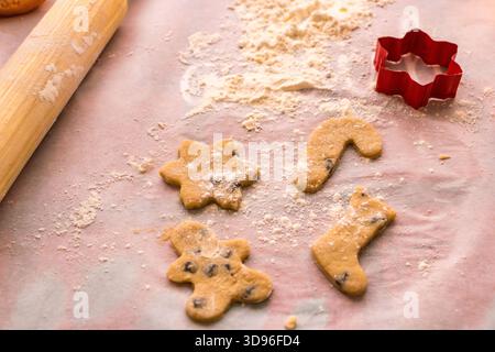 Homemade Christmas cookie preparation with dough, flour, cookie cutters and festive decorations on a kitchen table. Stock Photo