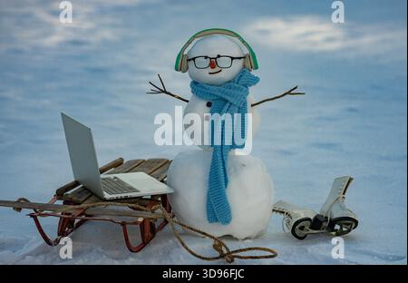 Funny winter snowman working on computer. Snowman using laptop outside. Remote online work winter concept. Winter snowman typing on laptop in snow. Stock Photo