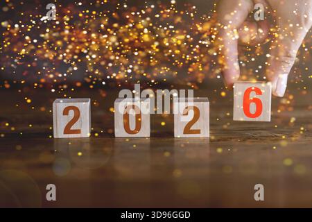 Happy New Year 2026 concept banner. Hand holding number 6 on wooden cube, isolated on bokeh background. Stock Photo