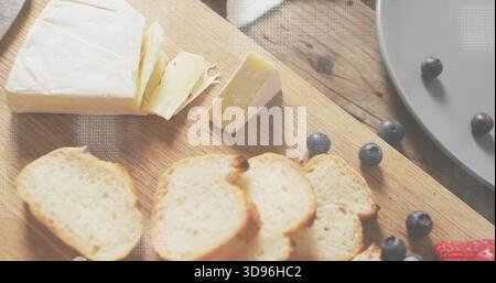 Displaying brie wedge resting on wood cutting board, with toasted crostini and loose blueberries Stock Photo