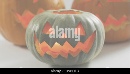 Glowing gray-green ribbed carved pumpkin emitting warm glow on tabletop, with blurred pumpkins Stock Photo