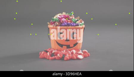 Displaying orange pumpkin bucket spilling foil candies and red-and-white sweets on gray tabletop Stock Photo