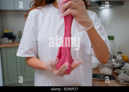 Woman manually stretching and kneading vibrant pink mochi dough with gloved hands, demonstrating the texture of sweet japanese rice cake during preparation in a clean kitchen Stock Photo
