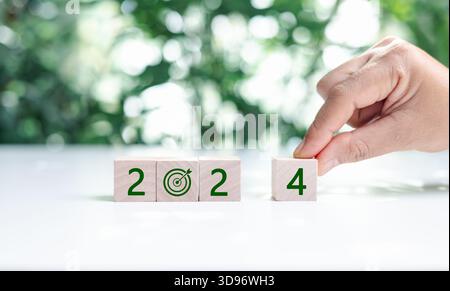 2024 numbers and earth care symbol on circle eco wooden blocks on wood table, green leaves background. Happy new year 2024 with the world care. Green Stock Photo
