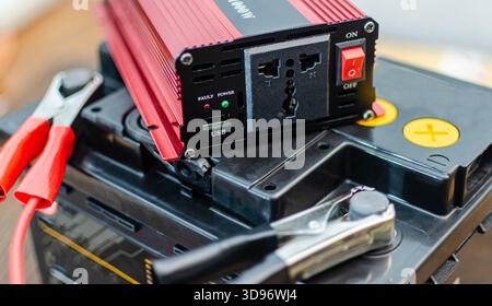 A close-up shot of a  red and black power inverter connected to a car battery using heavy-duty jumper cables with alligator clips. The inverter featur Stock Photo