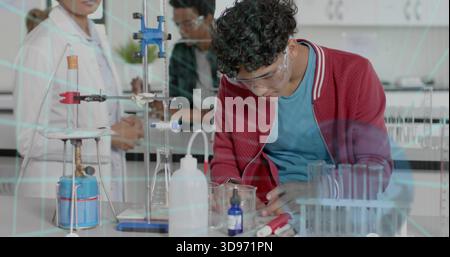 Leaning teen male wearing goggles and red jacket measuring beaker at school lab, with burner Stock Photo