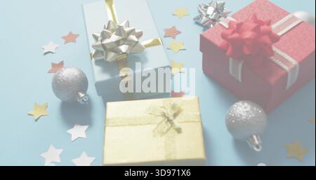 Showing three wrapped gift boxes sitting on pale blue table, with metallic bows and silver baubles Stock Photo