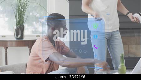 Reaching seated man wearing tee and jeans using hologram controls at home, standing with smartphone Stock Photo