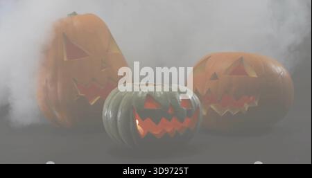 Glowing three carved pumpkins emitting warm inner light on dark tabletop with drifting smoke Stock Photo