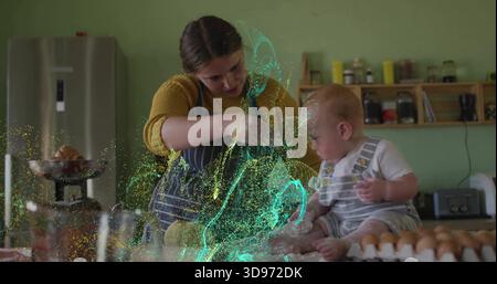 Mixing woman wearing striped apron with baby on kitchen counter cracked eggs and green-blue glow Stock Photo