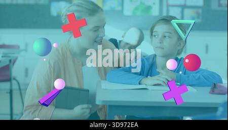 Kneeling teacher in peach cardigan guiding student in classroom holding tablet open workbook shapes Stock Photo