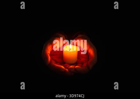 Burning candle in the mans hands on a dark background. Religious concept. Selective focus. Stock Photo