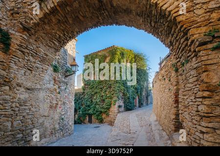 Stone wall facade featuring an arched, barred window, small upper windows, a street lamp in Peratallada, Spain Stock Photo