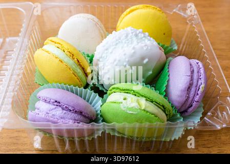 A few colorful French macarons in the transparent plastic container on the table, closeup. Stock Photo