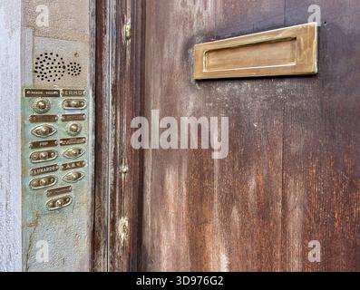 Old,vintage apartment intercom doorbell panel & a brass mail slot mounted on wooden door,common in multi-unit properties.Multiple buttons & nameplates. Stock Photo
