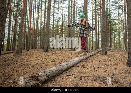 Woman walking on fallen tree log in middle of autumn pine forest, enjoying time outside on weekend. Stock Photo