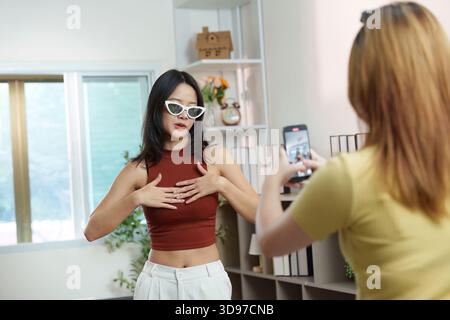 Social Media. A young woman showcasing her outfit while her friend records her indoors. Stock Photo