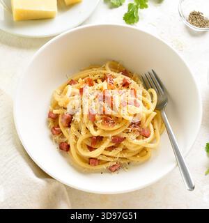 Italian pasta dish with crisp pancetta, parmesan cheese and black pepper in white ceramic bowl on light background. Close up view Stock Photo