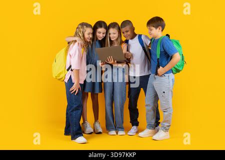 Preteen pupils standing close together with laptop, smiling and exploring digital learning Stock Photo