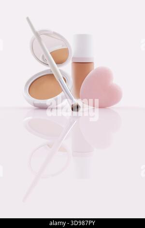 Opened compact powder, and a closed foundation in a pump bottle, soft brush and a heart shaped makeup puff. Cosmetics beauty products isolated on a gl Stock Photo