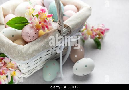 Colorful easter eggs and spring flowers overflowing from a white wicker basket on a light background Stock Photo
