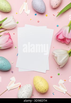 Easter greeting card mockup surrounded by colorful eggs, tulips, and bunny ears on pink background is perfect for spring celebrations Stock Photo