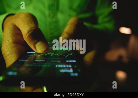 Hand typing on a smartphone displaying a financial chart for stock market trading Stock Photo