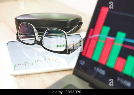 Glasses resting on a tablet displaying a financial chart and a buy button Stock Photo