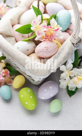 Colorful easter eggs and spring flowers overflowing from a white wicker basket on a table, celebrating easter holidays Stock Photo