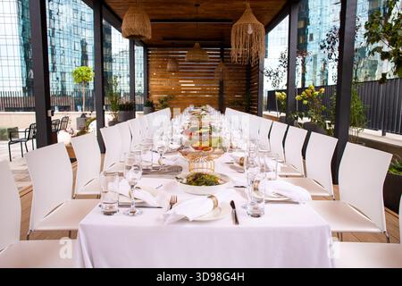 Long set table on terrace with city view - elegant table setting for event. Stock Photo