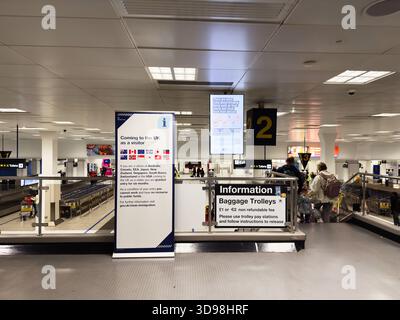 Manchester, UK - November 07, 2025: Busy Manchester airport scene with information signs, baggage trolleys, and travelers. Stock Photo