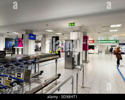Manchester, UK - November 07, 2025: Bustling Manchester airport scene with luggage, carts, and travelers at service desks and signs. Stock Photo
