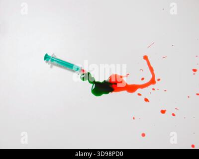 Syringe Pouring Green Paint Into Red Smear On White Surface, Color Mixing In Motion, Viscous Liquids Merging Stock Photo