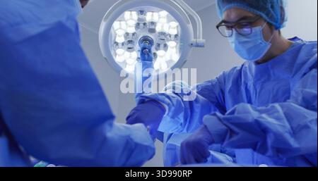 Operating surgical team wearing blue gowns, masks, gloves, working in operating room with LED light Stock Photo