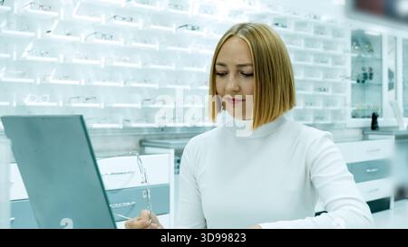 Female optician works on a laptop at a desk in the optical store Stock Photo